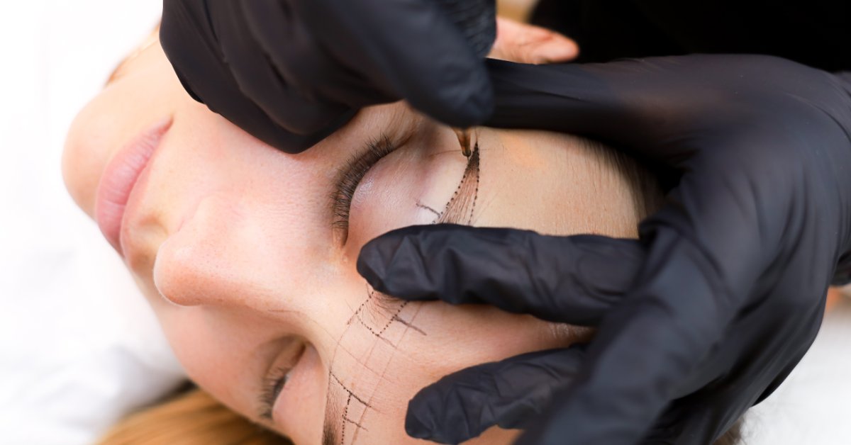 A woman's face who is receiving a permanent eyebrow makeup procedure from a qualified technician's hands.
