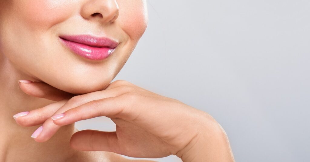 A woman holding her hand up under her chin showing off her lips that have a permanent lip blush on them.
