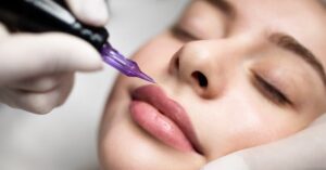 A woman laying down with her eyes closed receiving a lip blush procedure from the gloved hands of a professional.
